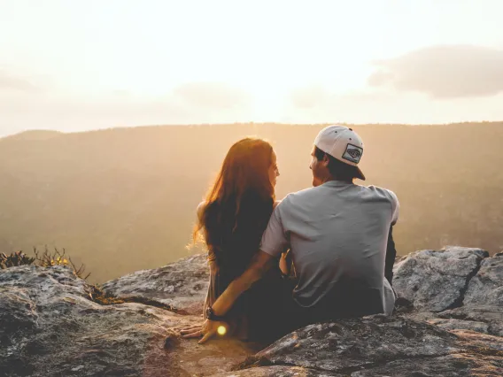 Two people sittng on a rock talking overlooking wilderness