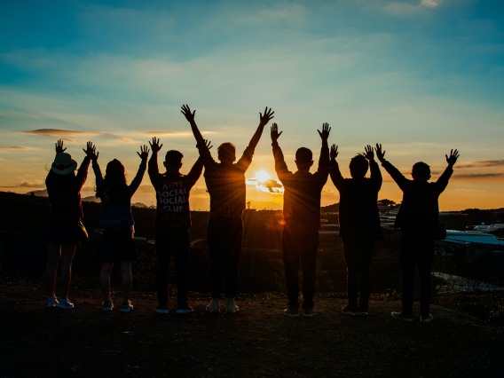 Silhouettes of people wathing sunset with arms up