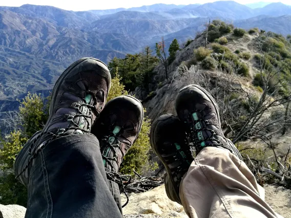 Two people's feet with hiking boots on and mountains in the background