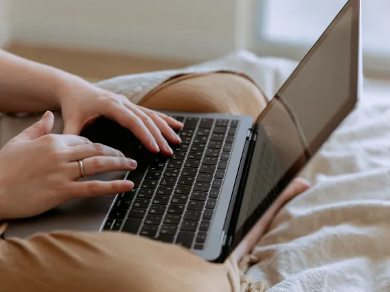 Laptop on a persons lap sitting in a bed