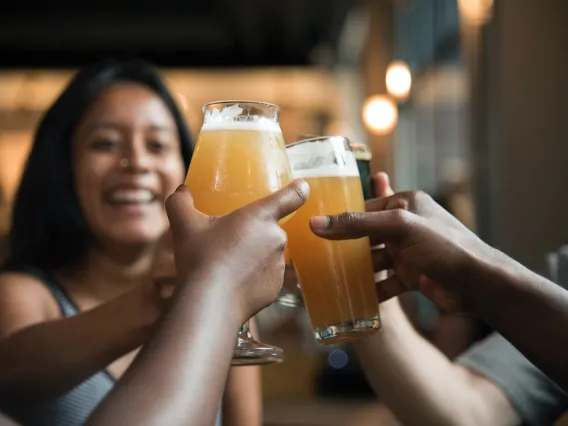 Hands holding beer glasses toasting with person in background smiling