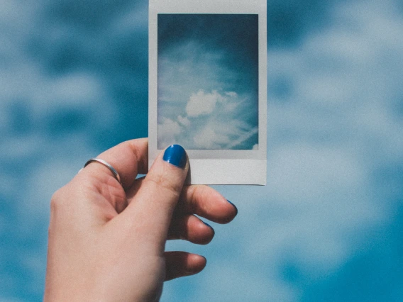 view of a person's hand holding up a photograph of the sky against the sky