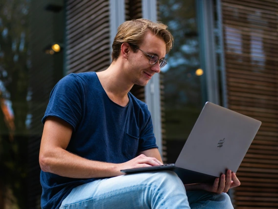 Male student sitting outside on laptop