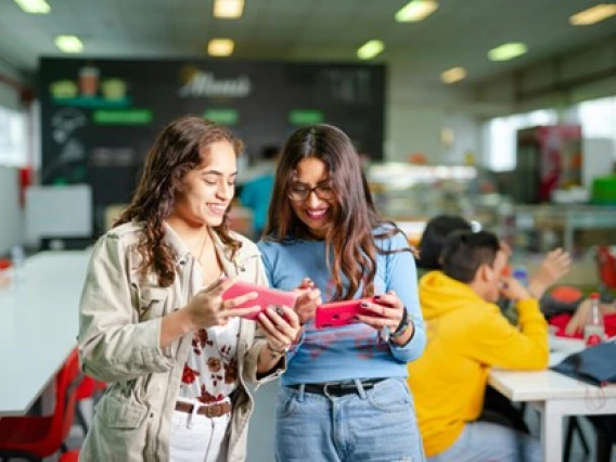 Two people with long hair smiling and looking at each other's phones with pink covers