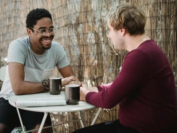 Two people with short hair having a conversation with coffee mugs on the table.