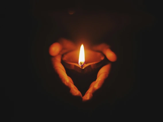 Hands holding a lit candle with dark background. 
