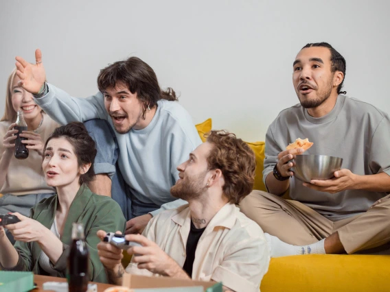 group of friends playing a video game and eating snacks on a couch