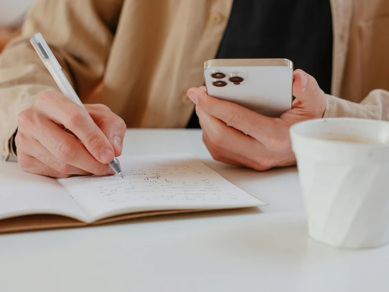 close-up of a person holding a phone and taking notes in a notebook
