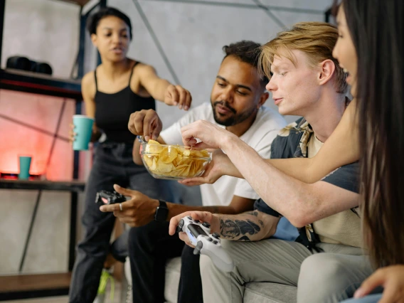 group of friends sitting on a couch eating chips and playing video games