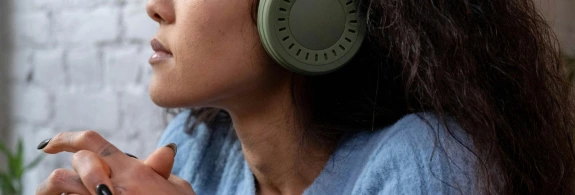 Person with blue sweater and long curly hair wearing green headphones