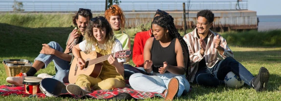 Group of people having a picnic on grass with someone playing guitar