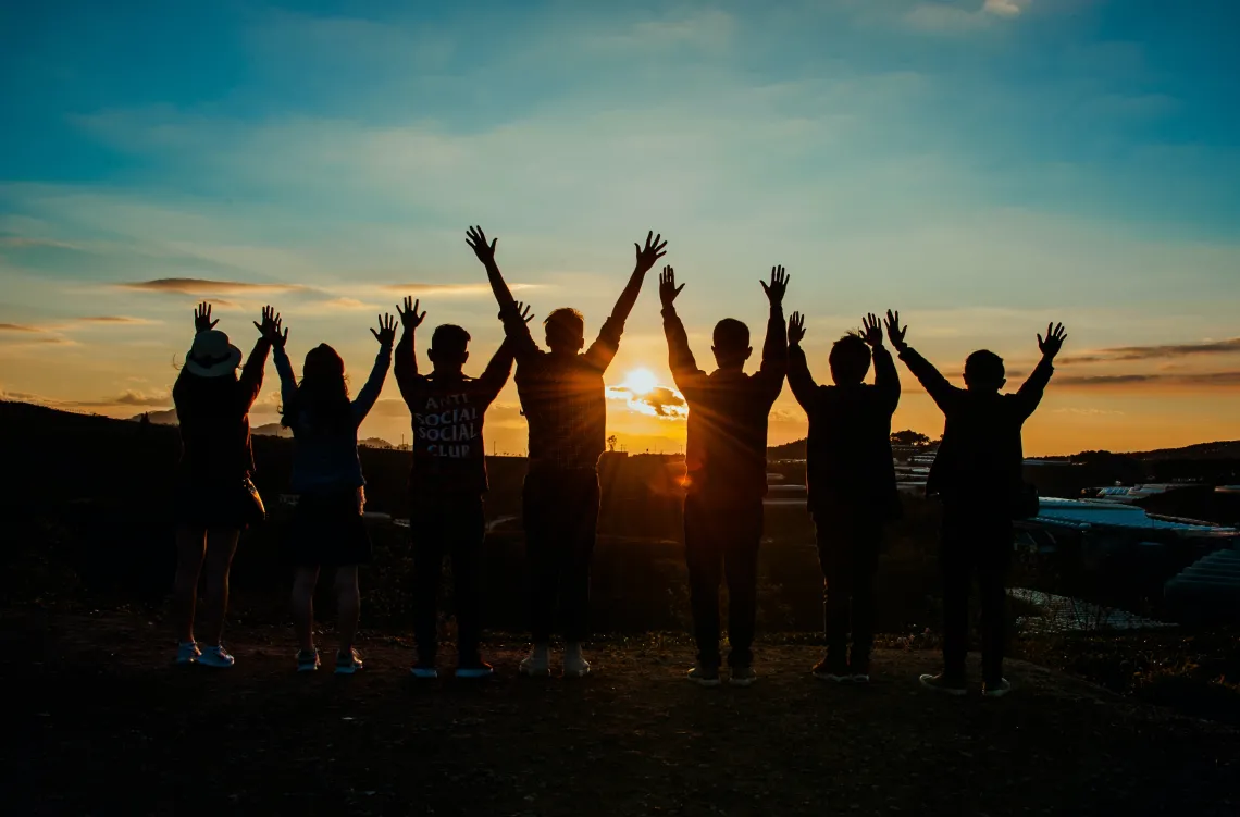 Silhouettes of people wathing sunset with arms up