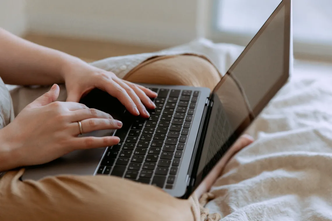 Laptop on a persons lap sitting in a bed