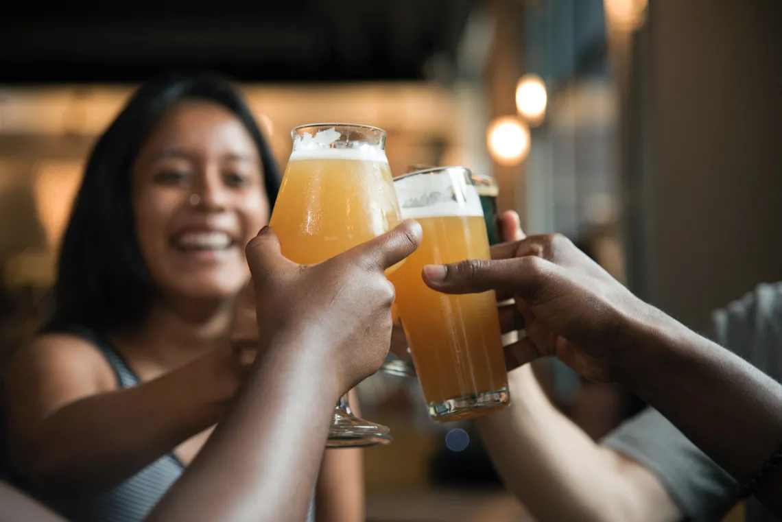 Hands holding beer glasses toasting with person in background smiling