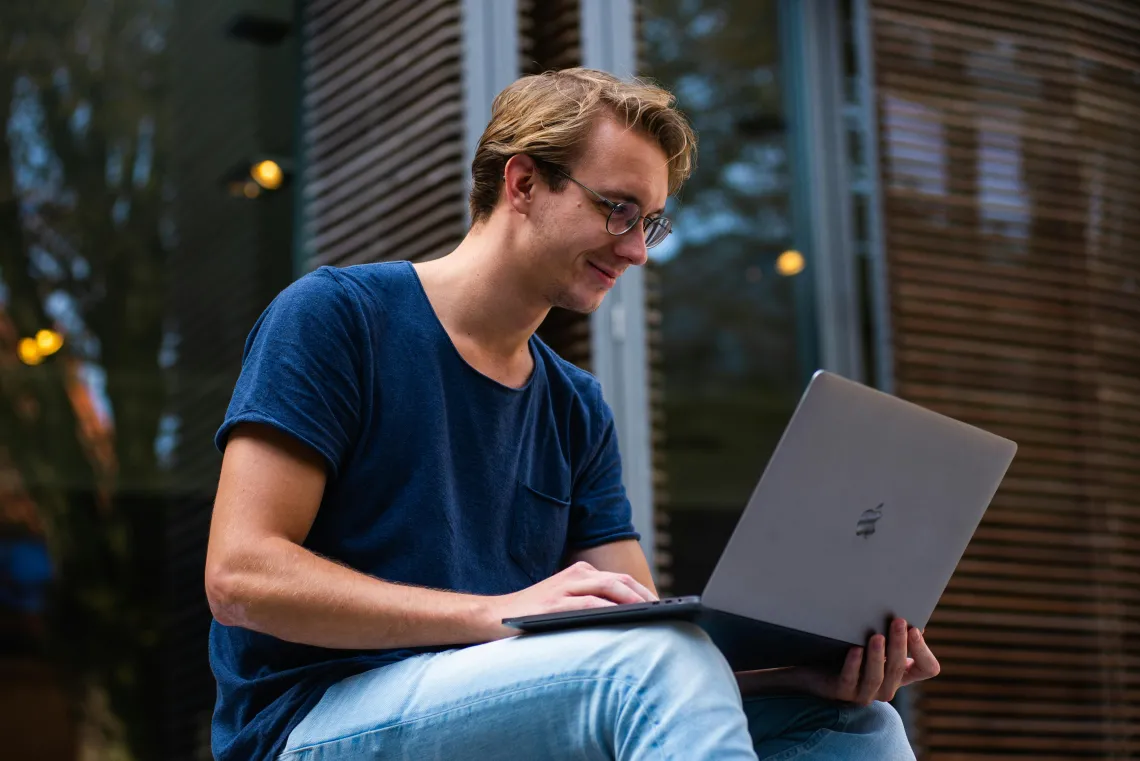 Male student sitting outside on laptop