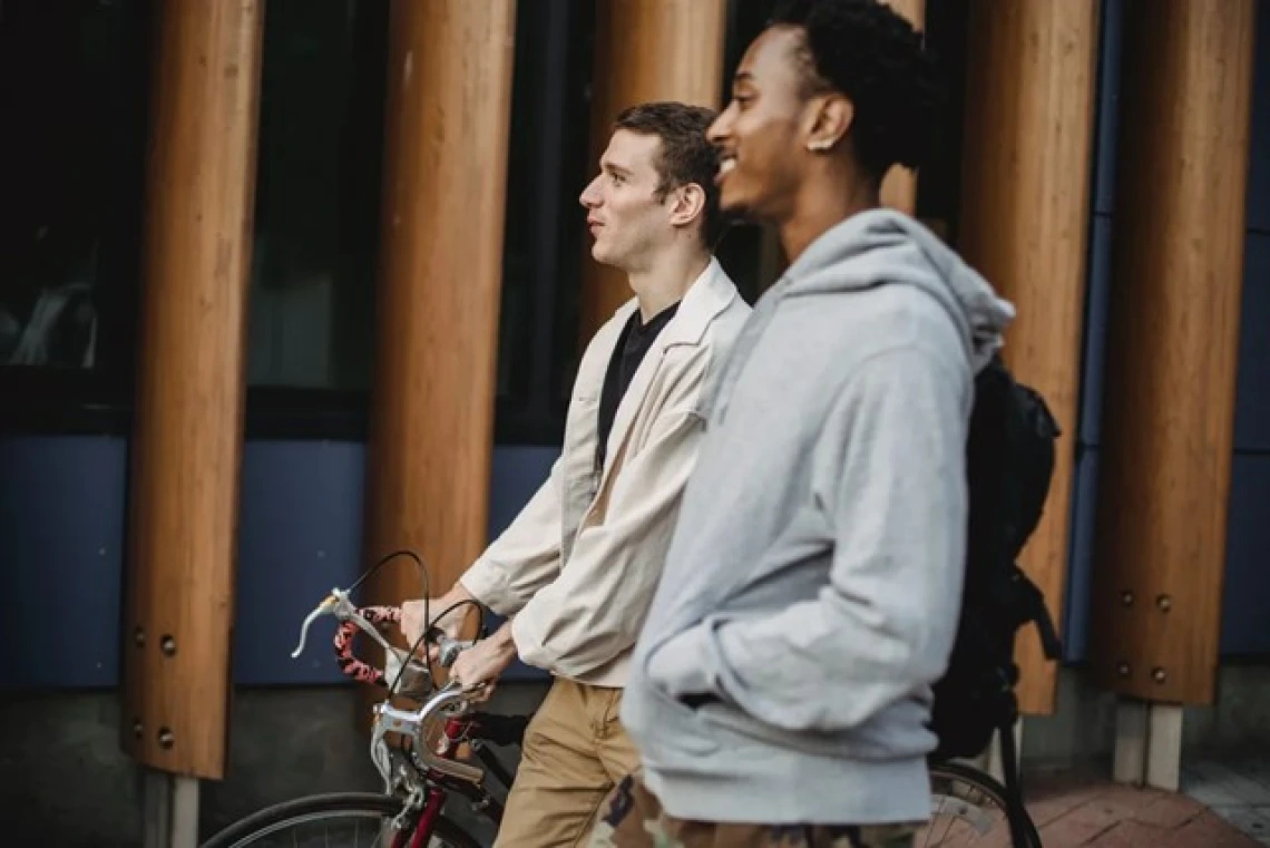 Two people walking along side each other and one is holding a bike