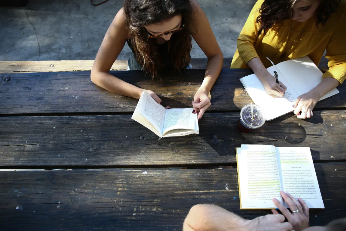 3 students with books/notebooks on picnic table
