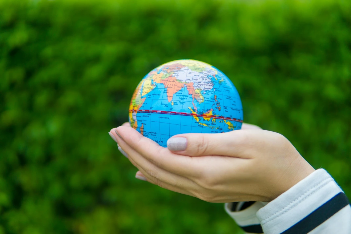 World globe being held by two hands with green background. 