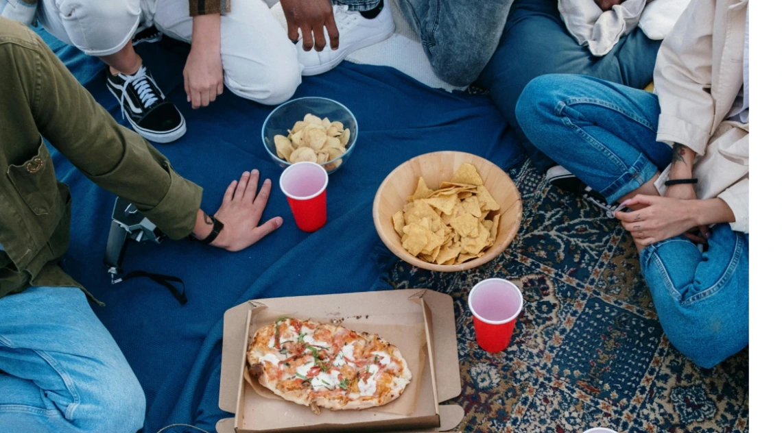 People sitting around on rugs, blankets eating pizza and popcorn with drinks in red cups.