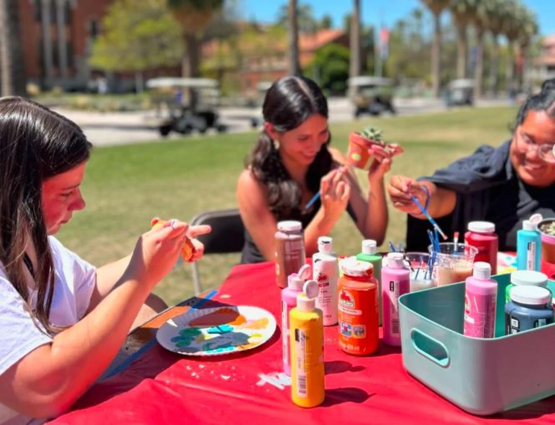 3 students smiling and painting outside on the mall