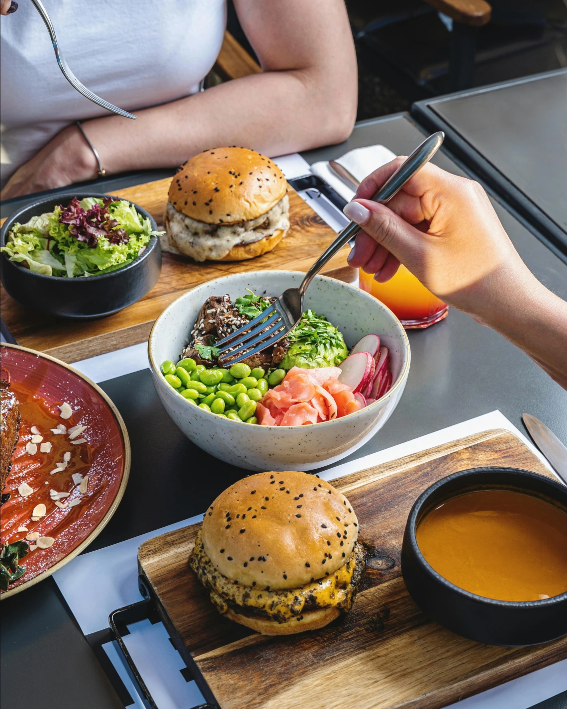 two plates with burgers, soup, salads