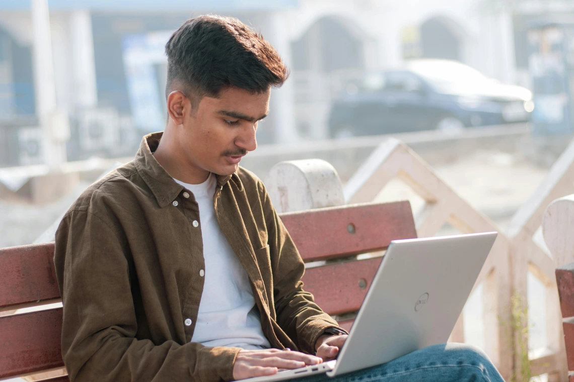 male sitting on a bench on computer