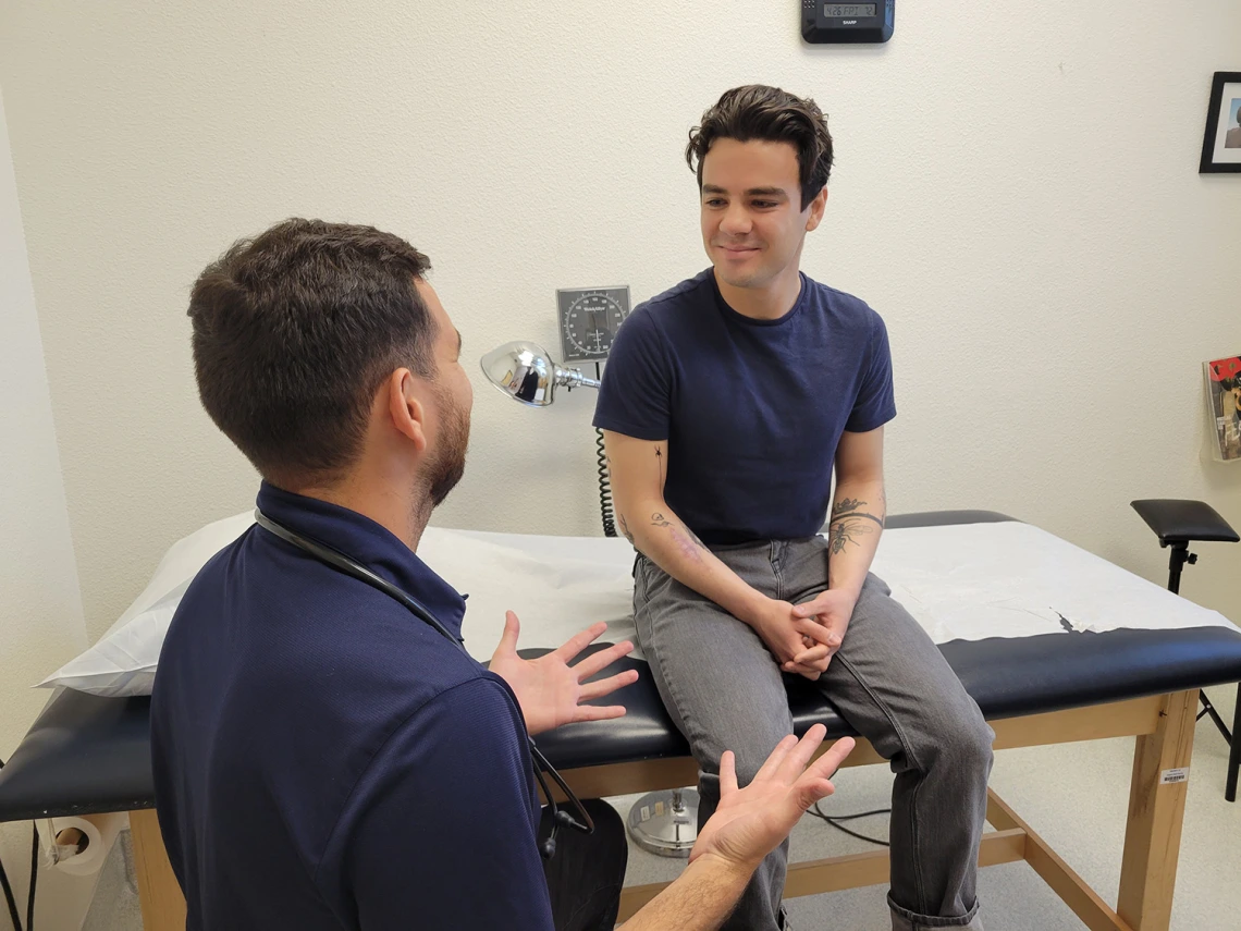 male student in doctors office smiling and talking with doctor