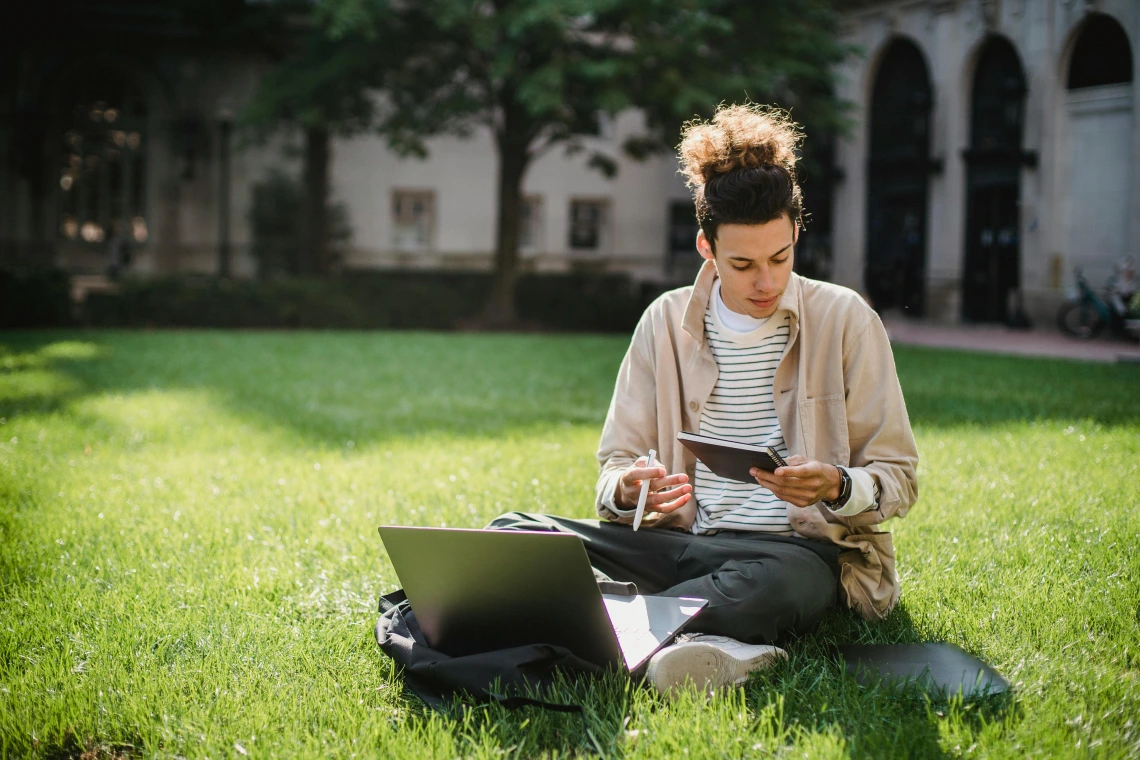 person sitting in the grass with a laptop computer and notebook