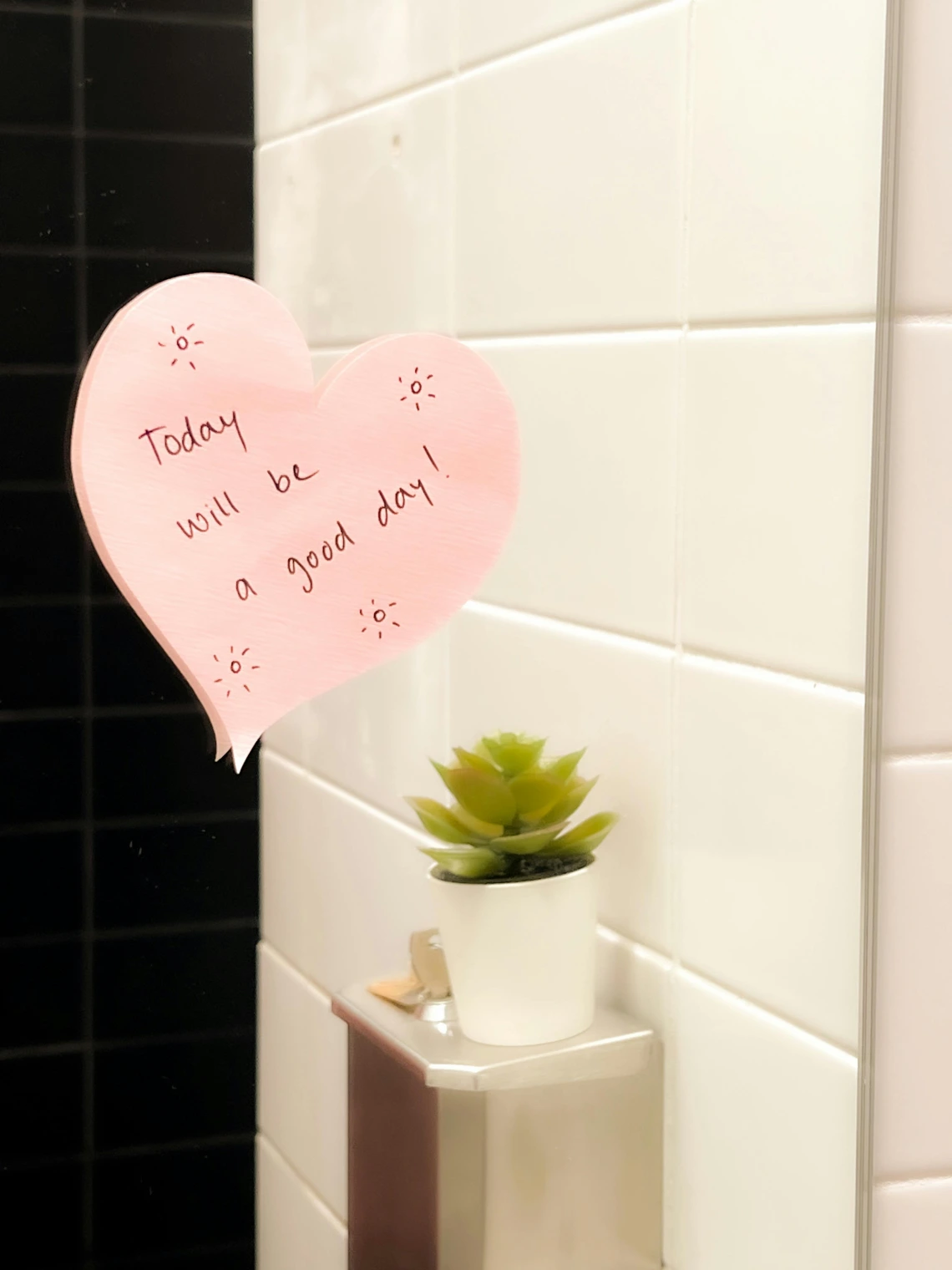sticky note in the shape of a heart on a bathroom mirror saying "today will be a good day"