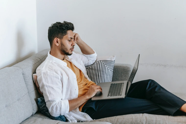 Male sitting on couch with open laptop on lap